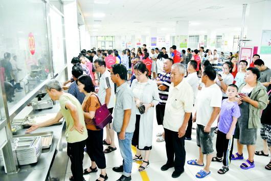 8月12日,在寿光市现代中学东校区安置点,受灾安置群众在食堂排队打饭.