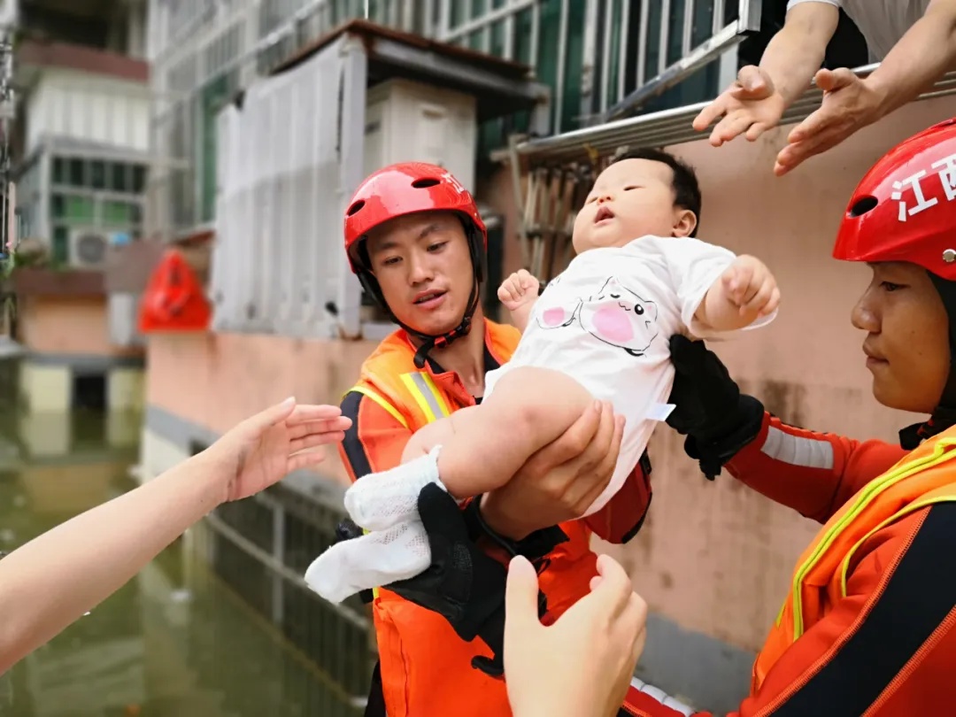 7月9日，江西省景德镇市茶山路有一名女子带着7个月大的婴儿，被洪水困在家中3天，消防员到达现场后，从窗口接力将婴儿抱出。（图片来源：应急管理部消防救援局）